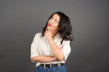 Güzel esmer kadın düşünüyor. Gri arkaplanda duruyor. 