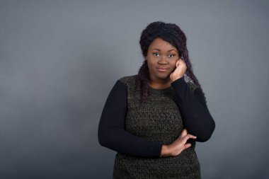 Neşeli, güzel, Afro-Amerikan kadın resmi. Günlük giysiler içinde gri duvarın karşısında duruyor. Yüzü birbirine yakın. İyi haberleri dinledikten sonra kameraya mutlu bir ifadeyle bakmak. Kendine güvenen kız..