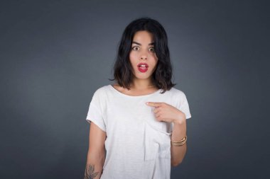 Şaşırmış güzel kız öğrenci sersemlemiş durumda, şaşkın bir şekilde kendini parmağıyla işaret ederek 
