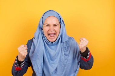 Güzel, orta yaşlı, tesettürlü Müslüman kadının portresi kameraya heyecanla bakıyor, ellerini başının üstüne kaldırıyor, beklenmedik bir şey fark ediyor, duvarın üzerinde izole edilmiş.. 