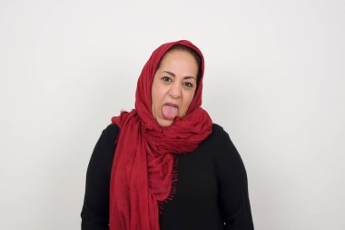 Vücut dili. Gri duvara karşı poz veren, suratını asan, bir şeye karşı hoşnutsuzluk gösteren olgun, stresli Müslüman kadın..