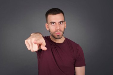 Kapalı mekandaki günlük giysiler içindeki neşeli genç adam fotoğrafı size mutluluğu gösteriyor, rekabeti seçiyor, olumlu bir ifadeye sahip. Yakışıklı zeki öğrenci, gri duvarda izole edilmiş bir şekilde seçim yapar.