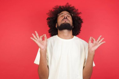 Kızıl duvarda meditasyon yapan afro saçlı genç bir adam. 