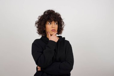 Tarz sahibi genç Avrupalı bir kadının tasvir edilmiş portresi, elleri çenesinin altında ve yana bakıyor şüpheli ve şüpheci bir ifadeyle, endişe ve şüpheyle. Gri arka planda kapalı duruyor..