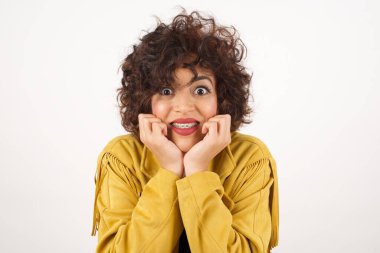 Hayalperest genç kadın ellerini çenesinin altına bastırıyor, mutlu bir ifadeyle bakıyor, dişlek gülüşü var, gri arka planda soyutlanmış.