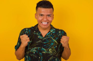 Güçlü, başarılı, kararlı İspanyol bir erkeğin portresi. Günlük tişörtler giymiş, kollarını kaldırmış, yumruklarını sıkmış, sevinç ve heyecanla haykırıyor. Zafer, başarı ve başarı kavramı.