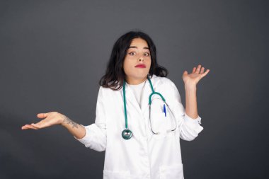 Güzel doktor kadın ifadeden şüphe ediyor, şaşırıyor ve merak ediyor, belirsiz bir gelecek omuz silkiyor, gri duvara karşı duruyor..