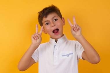 Sarı duvara karşı zafer işareti yapan sevimli çocuk.  
