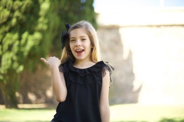 Omg konsepti. Şaşırmış, beyaz, siyah elbiseli, ağzı ve gözlerini kocaman açan, baş parmağıyla işaret eden, garip bir şey gösteren, beyaz, tatlı bir kız. 