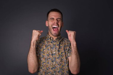 Kafkasyalı esmer adam başarısını ve zaferini sevinçle kutluyor ve yumruklarını zevkle sıkıyor. Hedefine ve hedeflerine ulaşmaktan mutlu olan şanslı bir adam. Olumlu duygular, duygular.