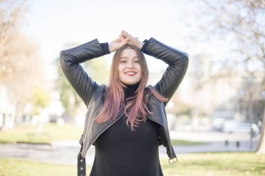 Genç, güzel, beyaz tenli esmer kadın bahar parkında rahatlıyor ve gülümsüyor.