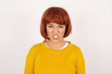 Çılgın deli kadın dişlerini öfkeyle sıkar, gelen sesten rahatsız olur, şık kıyafetler giyer, gri arka planda izole olur. Olumsuz duygu kavramı.