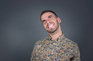 Esrarengiz bir gülümsemeyle yukarı bakan gizemli sarışın erkek portresi. Yakışıklı, gülümseyen adam gri duvara bakıyor..