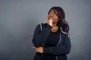 Yüz ifadeleri ve duygular. Düşünceli, hoş, Afro-Amerikalı bir kadın gündelik giysiler içinde kafasının altında el ele tutuşuyor, şüpheli bir şekilde bakıyor ve arkadaşının doğum günü partisinde ne giyeceğine karar veremiyor. 