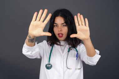 El hareketli parmak çerçevesi. Gülümseyen genç bir doktorun portresi. Kameraya bakıyor ve el hareketleriyle içeride duruyor..