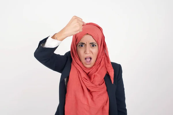 非常自信漂亮的穆斯林女人穿着黑色夹克 头戴头巾 手握拳头 好像随时准备战斗或挑战 尖叫着 脸上带着咄咄逼人的表情 在灰蒙蒙的背景上与世隔绝 — 图库照片