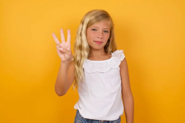 Χαριτωμένο Νεαρό Ξανθό Κοριτσάκι Κατά Κίτρινο Φόντο Στούντιο Δείχνει Τρία — Φωτογραφία Αρχείου