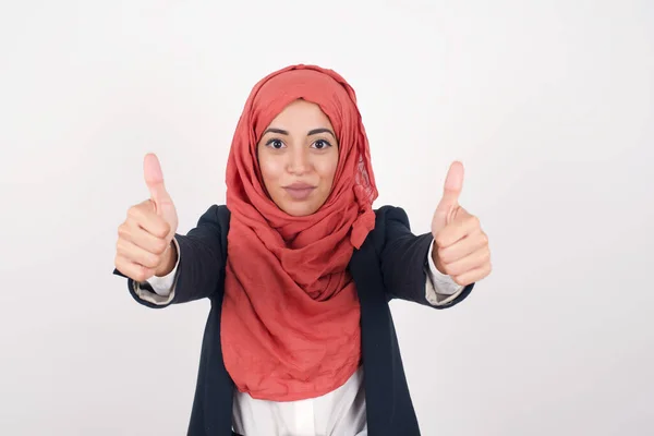 よくやった 幸せな美しいイスラム教徒の女性の肖像画は 黒いブレザーとヒジャブを着て 屋内で立っているジェスチャーを2つの親指を与えます ポジティブな人間の感情の表情ボディ言語 おかしい女の子 — ストック写真