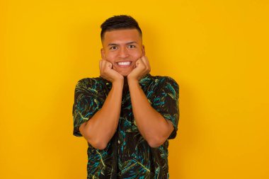 Hayalperest genç İspanyol adam ellerini çenesinin altına bastırıyor, mutlu bir ifadeyle bakıyor, dişlek gülüşü var, arka planda soyutlanmış.