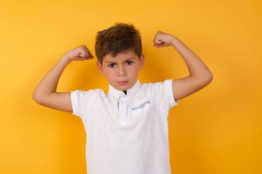 Sarı duvara karşı kaslarını gösteren sevimli çocuk.  