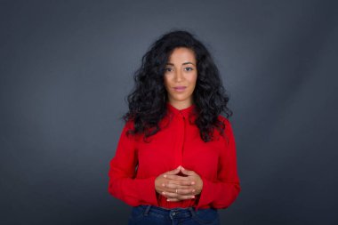 Kıvırcık saçlı, kırmızı tişörtlü, kendine güvenen yüzü gri arka planda olan yakışıklı esmer kadın portresi..