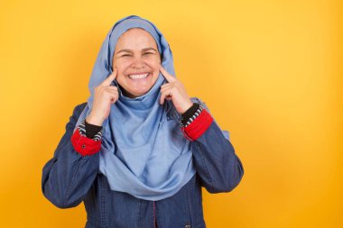 Orta yaşlı tesettürlü Müslüman kadının mükemmel beyaz dişlerini gösteren ışıl ışıl gülüşü, arka planda izole edilmiş portresi..