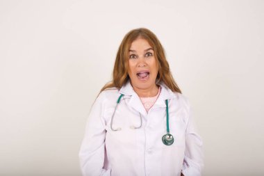 İnsanlar ve ani tepki kavramı. Şaşırmış Kafkasyalı olgun kadın doktor, omuz silkiyor, yana bakıyor, arkadaşlarıyla yeni planları için mutlu ve heyecanlı. Gri duvarda izole edilmiş..