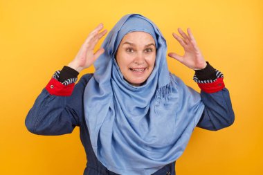 Güzel, orta yaşlı, tesettürlü Müslüman kadının portresi kameraya heyecanla bakıyor, ellerini başının üstüne kaldırıyor, beklenmedik bir şey fark ediyor, duvarın üzerinde izole edilmiş.. 