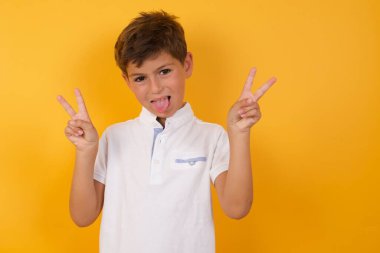 Dilini gösteren sevimli çocuk ve sarı duvara karşı zafer işareti.  