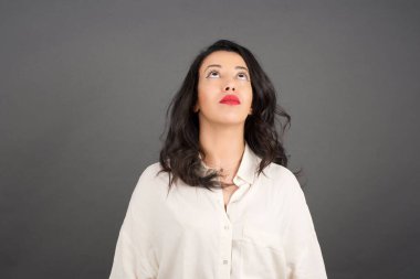 Gayri resmi giyinmiş güzel esmer kadın yukarı bakıyor. Gri arkaplanda duruyor. 