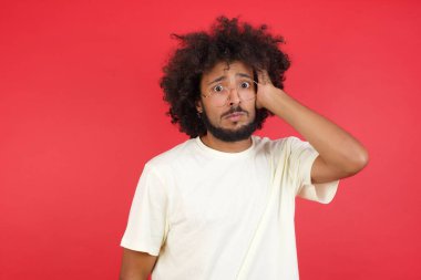 Afro saçlı genç adamın kırmızı duvara karşı kafası karışık.   