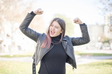 Deri ceketli beyaz bir kadın parkta kutlama yapıyor.  