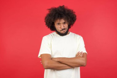 Kızıl duvara karşı kollarını kavuşturmuş afro saçlı genç bir adam.   