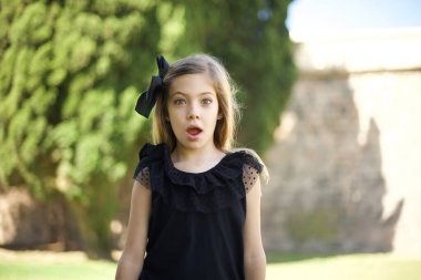 Siyah elbiseli çekici bir genç kız ağzı açık, ağzı açık ve ağzı açık bir şekilde şaşkın bir şekilde arkadaşının hikayesini dinlerken 