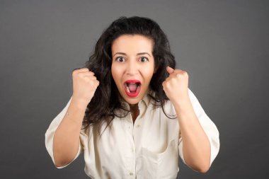 Sıradan giyinmiş güzel esmer kadın kızgın. Gri arkaplanda duruyor.  