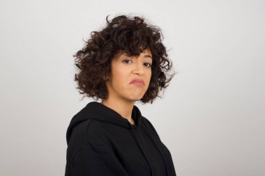 Züppe ifadeli güzel bir kadın dudaklarını kıvırıyor ve kaşlarını kaldırıyor şüpheli ve şüpheci bir ifadeyle şüpheli ve şüpheci bir ifadeyle bakıyor. Gri arka planda kapalı duruyor..