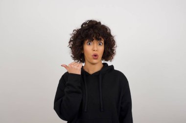 Genç ve neşeli kadınların başparmak ucunda yatay çekimleri beyaz arka planda izole edilmiş boş bir duvara işaret ediyor. Şuna bir bak. Etnik konsept.