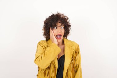 Yüzüne yan gözle bakan heyecanlı bir kadın. Gri arka planda heyecandan yana bakan mutlu genç bir kadın..