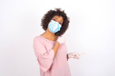 Yüz maskesi takan genç bir kadın ve beyaz arka planda izole edilmiş günlük giysiler.