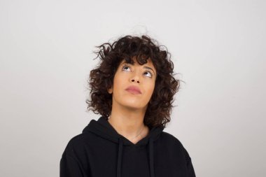 Düz saçlı, esrarengiz bir gülümsemeyle yukarı bakan kapüşonlu büyüleyici kadının portresi. Güzel gülümseyen kız, gri duvara bakıyor..