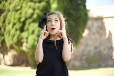 Güzel, zarif bir kızın portresi şaşırmış, şaşırmış görünüyor ve parmaklarıyla garip bir şey gösteriyor..