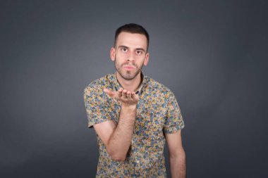 Sevimli çekici bir adam kameraya öpücük yolluyor, sevgilisine aşkını gösteriyor ya da uzaktan veda ediyor, gri stüdyo arka planında izole bir şekilde..