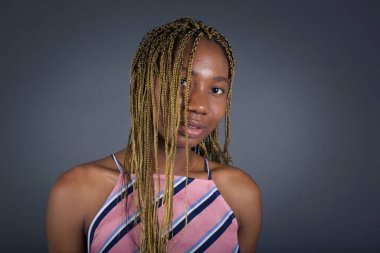 Güzel görünümlü Afro-Amerikan kadının yatay portresi. Yüzünü saçlarıyla örterek mutlu bir şekilde kameraya bakıyor..