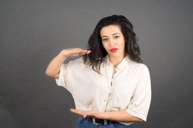 Gayri resmi giyinmiş güzel esmer kadın bir şeyler gösteriyor. Gri arkaplanda duruyor. 