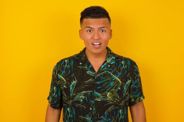 Çekici genç adam şaşırmış ve şok olmuş görünüyor, ağzı açık ve çenesi sarı duvara dayalı.