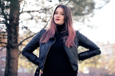 Parkta gülümseyen deri ceketli beyaz bir kadın.  