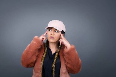 Hayalperest esmer kadın, düşünceli bir yüz ifadesi var, yüzünü çevirmiş, hoş bir şey düşünüyor, gri duvara karşı poz veriyor..