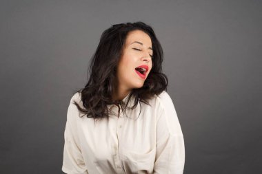 Güzel esmer kadın, ağzı açık gündelik giyinmiş. Gri arkaplanda duruyor. 