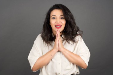 Gayri resmi giyinmiş güzel esmer kadın bir şey istiyor. Gri arkaplanda duruyor.  