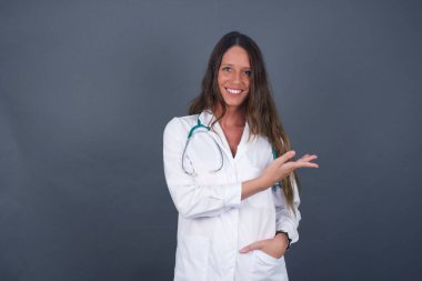 Pozitif memnun dişi der ki: Vay be, ne kadar heyecan verici, hayret verici bir ifade, boş uzayda bir şey gösteriyor, açık elle izole edilmiş gri arkaplan üzerinde. Reklam kavramı.